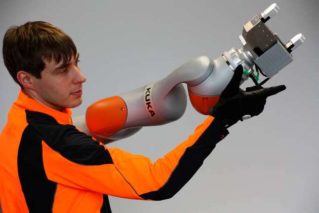 Co-CEO Georg Püschel steuert einen Roboter inklusive eines Greifers mit einer Sensorjacke und einem Sensorhandschuh.