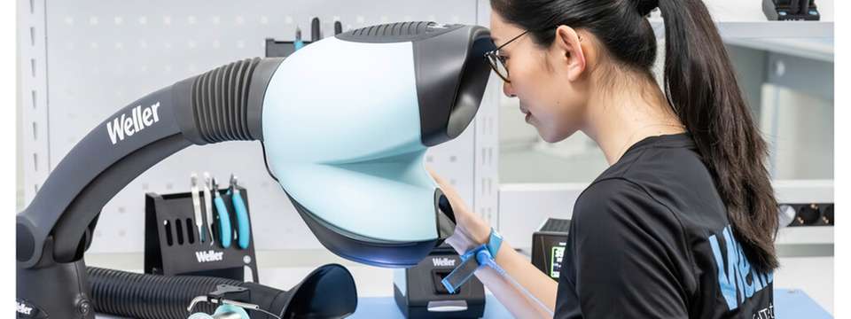 Mitarbeiterin prüft eine elektronische Baugruppe mit dem Prisma Mikroskop ESD an einem Weller-Arbeitsplatz.