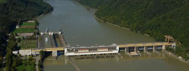 Luftaufnahme des Donaukraftwerks Aschach mit Wehranlage und Österreichs tiefster Donau-Schiffsschleuse, eingebettet in die enge Flusspassage zwischen bewaldeten Hängen.