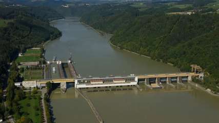 Luftaufnahme des Donaukraftwerks Aschach mit Wehranlage und Österreichs tiefster Donau-Schiffsschleuse, eingebettet in die enge Flusspassage zwischen bewaldeten Hängen.