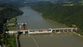 Luftaufnahme des Donaukraftwerks Aschach mit Wehranlage und Österreichs tiefster Donau-Schiffsschleuse, eingebettet in die enge Flusspassage zwischen bewaldeten Hängen.