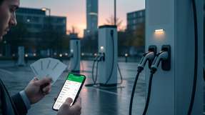 Laden unterwegs: E‑Auto an öffentlicher Ladesäule. Ein Fahrer hält mehrere Ladekarten; das Smartphone zeigt eine unübersichtliche Tarifauswahl.