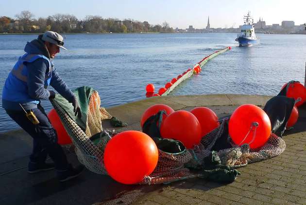 Das Crev Tranfer Vessel „Theron“ zieht die Netzsperre über die Kaikante in die Warnow. SBOIL Projektmitarbeiter Marcus Siewert von der Professur Geotechnik und Küstenwasserbau der Universität Rostock überwacht das Ablaufen an Land.