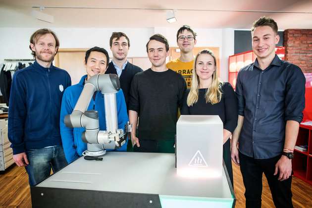 Das Wandelbots-Kernteam posiert vor einen Demonstrator, der eine Anwendung aus der Mikrochipindustrie zeigt.