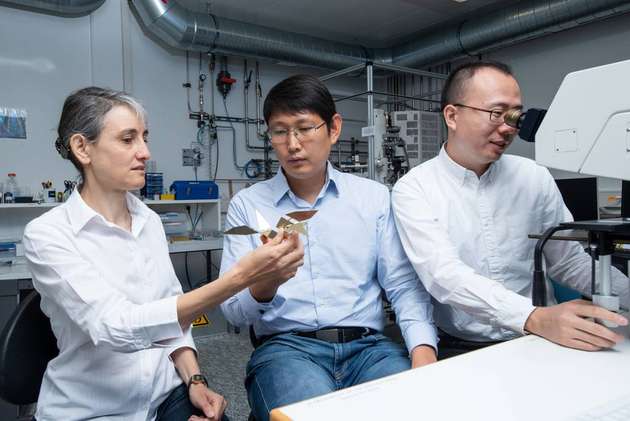 Laura Heyderman und Tian-Yun Huang, von links nach rechts, mit einem Modell des Origami-Vogels, während Jizhai Cui den echten Mikroroboter unter einem Mikroskop beobachtet.