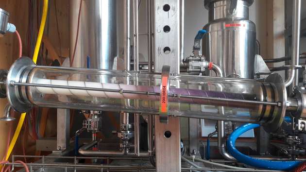 An den helixförmigen Einbauten im Reaktor bilden sich Turbulenzen, die für eine gute Durchmischung sorgen. Gleichzeitig schiebt sich die überlagernde Pfropfenströmung kontinuierlich durch die Röhre, hier mittels violetter Tinte dargestellt. So können Verweilzeit und Durchmischung jeweils für sich optimiert werden.