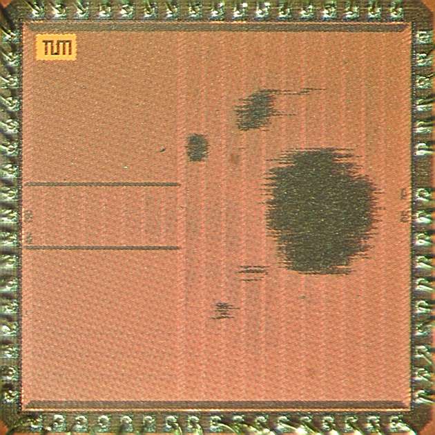 Fotografie des ASICs: Oben links stellt das TUM-Logo die korrekte Orientierung des Chips sicher. Am umlaufenden Bildrand befinden sich die Anschlüsse für Ein- und Ausgabedaten sowie die Stromversorgung. Zwei umrandete Bereiche in der linken Bildhälfte repräsentieren die Speicherblöcke des Chips. In der Mitte der rechten Bildhälfte, als Schattierung zu erkennen, liegt der Bereich der höchsten Schaltungsdichte. Hier wurden die Post-Quanten-Beschleuniger auf dem Chip platziert.