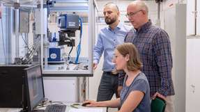 Dr. Janio Venturini (links), Prof. Tom Nilges und Erstautorin Anna Vogel stehen vor einem Messgerät zur Bestimmung von Kristallstrukturen, einem sogenannten Einkristalldiffraktometer.