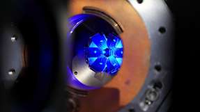 Blick auf eine Wolke von blau fluoreszierenden Strontiumatomen, die mithilfe von Laserstrahlen bis auf Temperaturen dicht am absoluten Nullpunkt gekühlt werden. Gut sichtbar ist der Kranz aus sechs Spiegeln, die die Strahlen reflektieren.