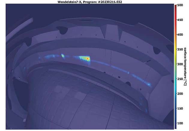 Infrarotaufnahme aus dem Vakuumgefäß von Wendelstein 7-X. Das Bild zeigt nicht das Plasma an sich, sondern die Temperaturverteilung an den wassergekühlten Divertor-Prallplatten. Die Divertor-Prallplatten werden zur Abführung der Wärme aus dem Plasma eingesetzt. Deutlich erkennbar ist eine definierte Linie im Zentrum, die sogenannte Strike Line. Dort berührt das Plasma den Divertor und die Temperatur ist am höchsten. In einzelnen Bereichen werden bis zu 600 °C erreicht (rote Flächen). Die Divertorkacheln können Temperaturen bis zu 1.200 °C aushalten.