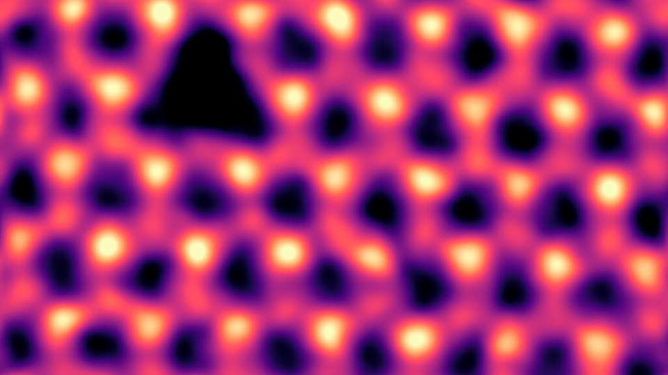 Einzelne Stickstoff-Leerstellen (dreieckiger dunkler Kontrast oben links), die durch Elektronenbestrahlung in hexagonalem Bornitrid erzeugt wurden. Gefiltertes und gefärbtes rastertransmissionselektronenmikroskopischen Bild.