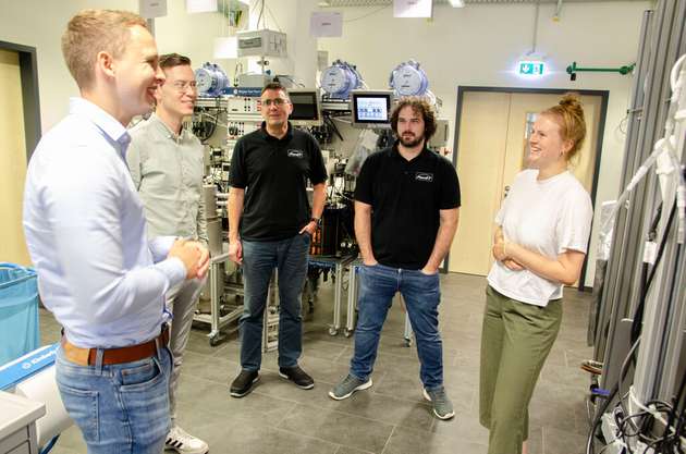 Im Technikum auf dem Steinfurter Campus der FH Münster zeigten Sören Kamphus (l.) und Juliana Rolf (r.) den Projektpartnern im Anschluss die bestehenden Anlagen zur Wasserstoffgewinnung, die in vorherigen Forschungsprojekten entstanden sind. 