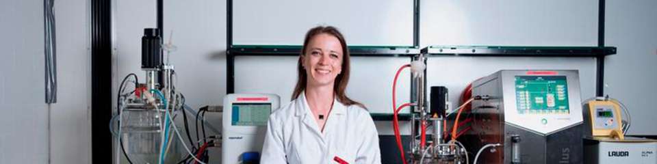 Carolin Mügge im Labor der Biotechnologie. Im Hintergrund sind Fermenter zu sehen, mit denen im Litermaßstab Zellen kultiviert und Biotransformationen durchgeführt werden können.