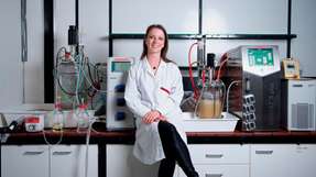 Carolin Mügge im Labor der Biotechnologie. Im Hintergrund sind Fermenter zu sehen, mit denen im Litermaßstab Zellen kultiviert und Biotransformationen durchgeführt werden können.
