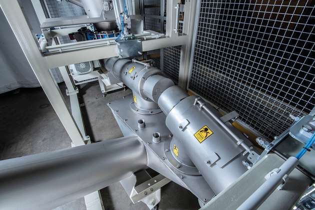Doppelte Big Bag Entleerstation als staubdichtes, geschlossenes System. Das Produkt wird über Sammelschnecken von den Entleerstationen in einen mittigen Sammelbehälter gefördert. Von dort aus geht es mit einer Austragsschnecke in Schrägstellung in die Produktion.