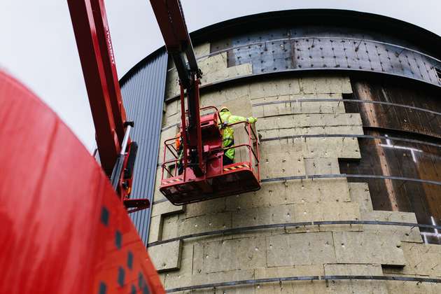 „Arbeiter montieren Dämmplatten an der Außenwand der Sandbatterie in Pornainen. Der Hochtemperaturspeicher wird für die CO2-arme Fernwärmeversorgung vorbereitet.