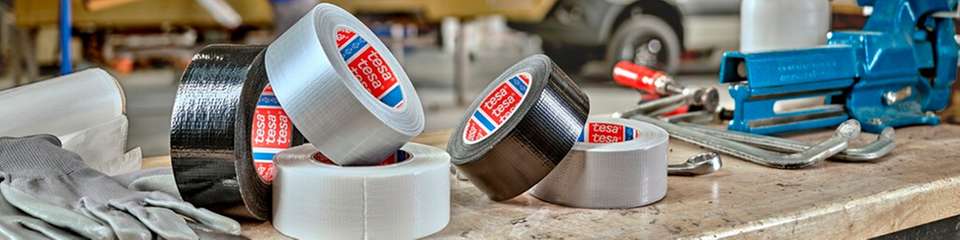 Tesa-Klebebänder in verschiedenen Ausführungen auf einer Werkbank – typische Einsatzmittel für Abdecken, Befestigen und Reparieren in industriellen und handwerklichen Anwendungen.