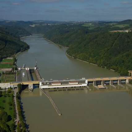 Luftaufnahme des Donaukraftwerks Aschach mit Wehranlage und Österreichs tiefster Donau-Schiffsschleuse, eingebettet in die enge Flusspassage zwischen bewaldeten Hängen.
