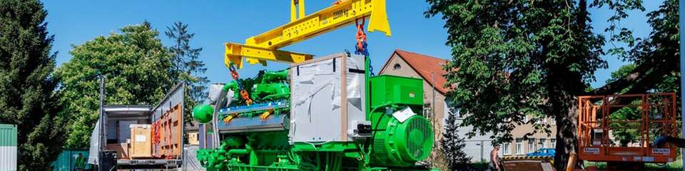 Der Gasmotor, der die KWK-Einheit der iKWK-Anlage Gera-Langenberg bildet, wird mit einem Kran vom Lkw heruntergehoben und für die Einbringung in das Heizhaus vorbereitet.