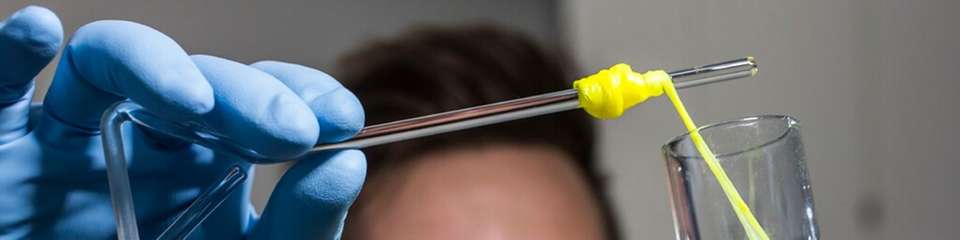 Ein Mitarbeiter zieht im Labor für Systembiotechnologie an der Universität des Saarlandes einen Bionylonfaden aus einem Glaskolben.