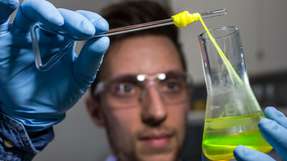 Ein Mitarbeiter zieht im Labor für Systembiotechnologie an der Universität des Saarlandes einen Bionylonfaden aus einem Glaskolben.