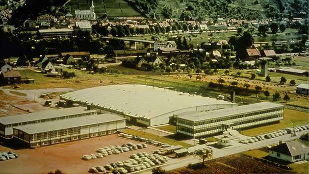 1965: Neue Firmenzentrale – Die verschiedenen Zweigbetriebe für Produktion und Verwaltung liegen weit verstreut, aus Platzmangel zum Teil in ehemaligen Schulgebäuden und Gaststätten. Das erschwert die Zusammenarbeit enorm. Seit 1960 werden daher am Ortsrand von Trennfurt zuerst neue Werkshallen, dann Verwaltungs-, Sozial- und Versandgebäude errichtet. Nun können alle Angestellten in der Alexander-Wiegand-Straße an einem Ort zusammenarbeiten.
