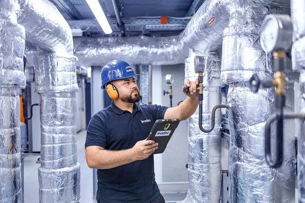 Ein Techniker kontrolliert Messstellen an isolierten Rohrleitungen und dokumentiert die Prüfung per Tablet.