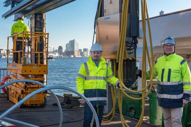 Sergej Nickel und Olaf Biesterfeldt (von links) von Vahle neben dem verfahrbaren Wagen des Landstromsystems auf einem schwimmenden Ponton im Hamburger Hafen.