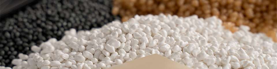 Verschiedene biobasierte Kunststoffgranulate in Schwarz, Weiß und Braun sowie eine helle Compoundplatte – Materialvielfalt für nachhaltige Verpackungsanwendungen.