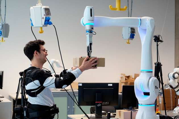 Forscher Federica Masiero nimmt ein Päckchen entgegen, dessen Gewicht der Roboter vorher bereits an das Exoskelett übermittelt hat. 