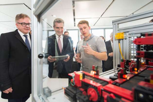 Lucas Fischer (rechts), bei Pilz Student der Dualen Hochschule Baden-Württemberg im Fach Elektrotechnik, zeigt dem EU-Kommissar (Mitte) wie mit Software von Pilz heute per Tablet ganze Anlagen sicher gesteuert werden können. 