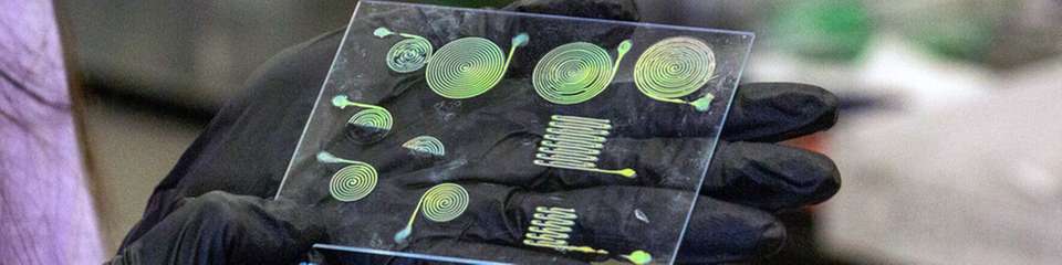 Alicia Ng, Doktorandin der Materialwissenschaften und des Ingenieurwesens, hält eine Reihe verschiedener Strukturen hoch, die aus einem neuen, 3D-gedruckten Material hergestellt wurden, das seine Farbe ändert, wenn es gedehnt wird.