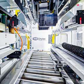 Die Anlage für den Pulverlackhersteller TIGER Coatings führt verschiedene Prozessschritte vollautomatisch durch – vom Verschließen des Innensacks über das Verkleben des Kartons, Wiegen und Etikettieren bis zur Palettierung.